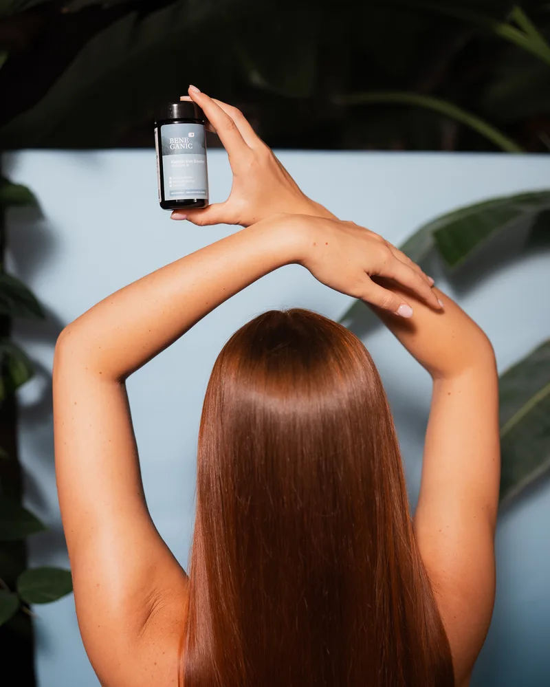 A woman with long, glossy hair holding a bottle of the Beneganic Keratin Hair Booster above her head