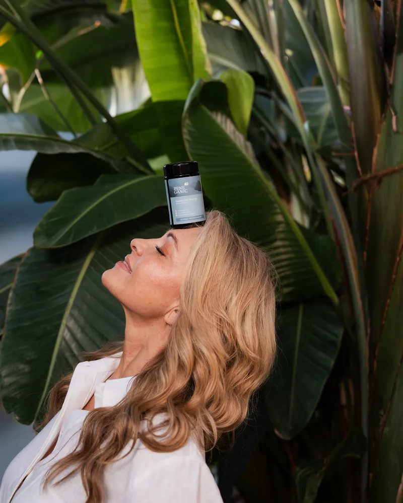 A woman tilting her head back with a bottle of the Beneganic Keratin Hair Booster balanced on her forehead
