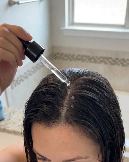 A woman applying Beneganic Intensive Hair Serum with a dropper along her part