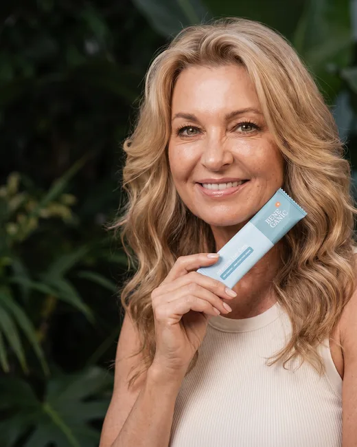 A woman holding a Beneganic Intensive Hair Care sachet near her face outdoors